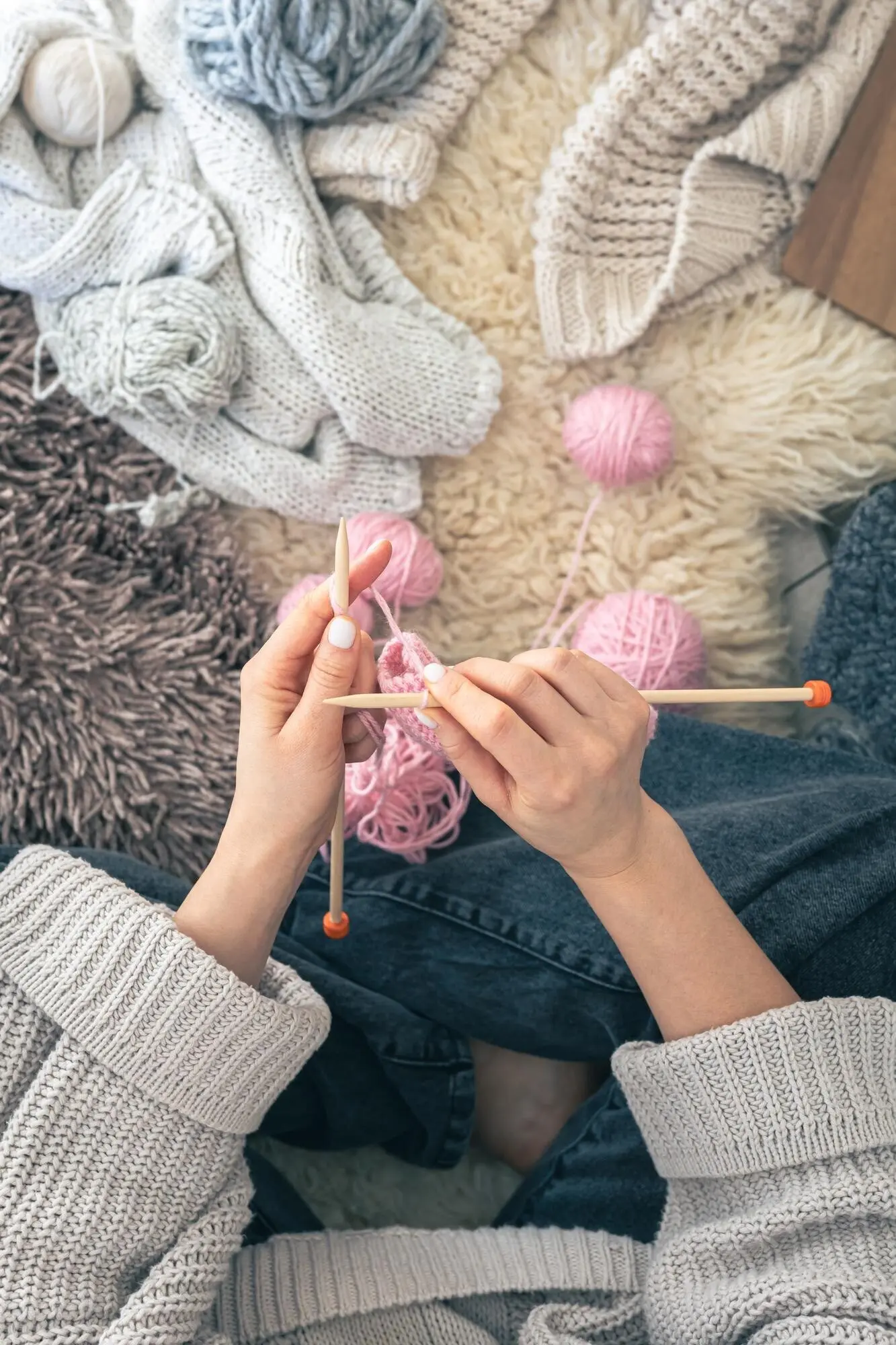 Weibliche Hände stricken zu Hause einen warmen pinken Schal, von oben gesehen.