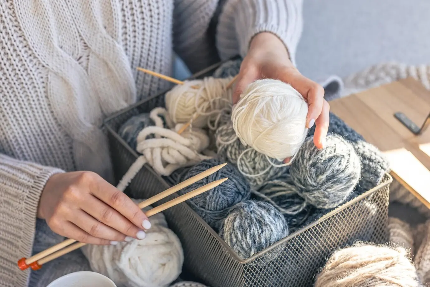 Hölzerne Stricknadeln und ein Garnknäuel in weiblichen Händen.
